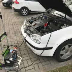 Awaryjny rozruch samochodu: podłączony wózek z akumulatorem do białego VW.