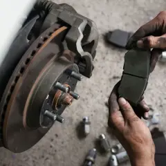 Mechanik trzyma nowe klocki hamulcowe, zastanawiając się, ile kosztuje wymiana klocków hamulcowych.