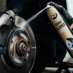 Czyszczenie hamulców: ręka w czarnej rękawiczce rozpyla preparat K2 Brake Cleaner na tarczę hamulcową.