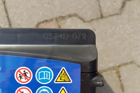 Na akumulatorze Exide widoczny kod C324D 079, który może oznaczać datę produkcji. Obok symbole ostrzegawcze.