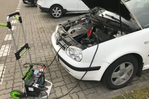 Awaryjny rozruch samochodu: podłączony wózek z akumulatorem do białego VW.