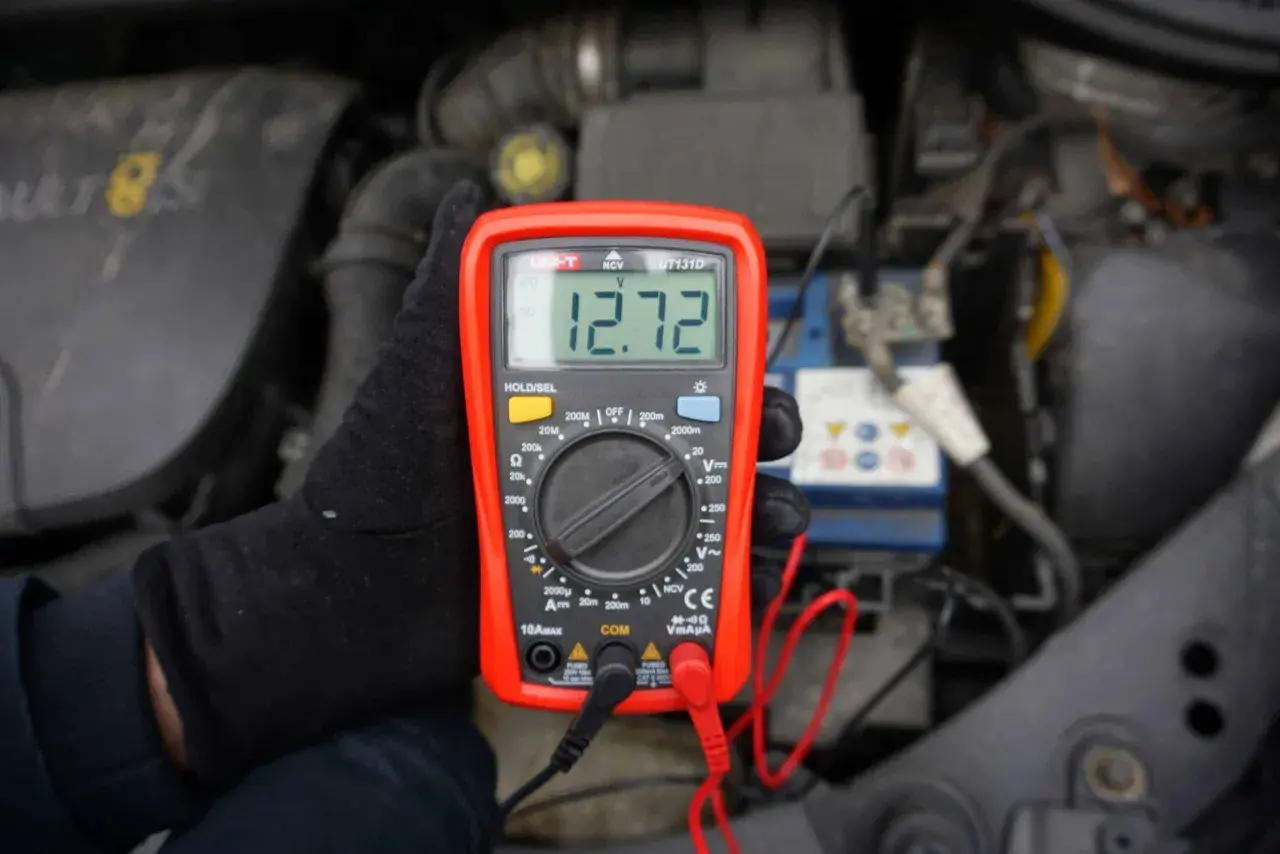 Multimetr pokazuje 12.72V. Sprawdzam, ile volt powinien ładować alternator, by upewnić się, że akumulator jest w dobrym stanie.