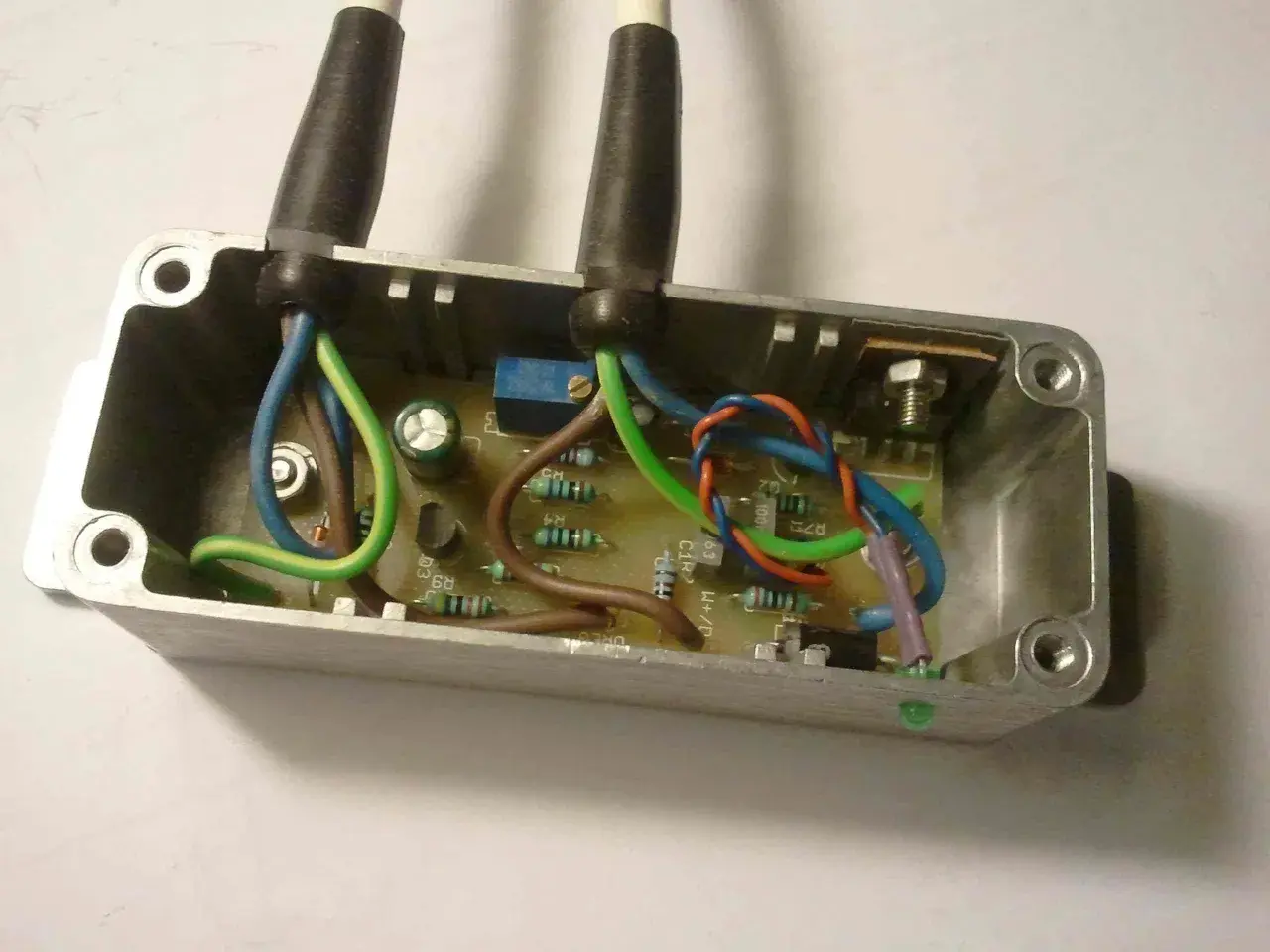 Schemat połączeń regulatora napięcia 12V. Widać płytkę drukowaną z elementami elektronicznymi i przewodami w metalowej obudowie.