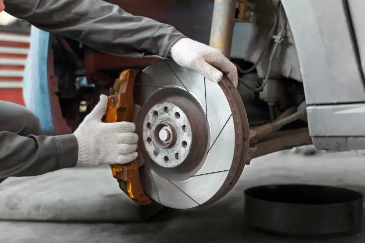 Mechanik w białych rękawiczkach wymienia tarczę hamulcową. Zastanawiasz się, ile kosztuje wymiana klocków hamulcowych?