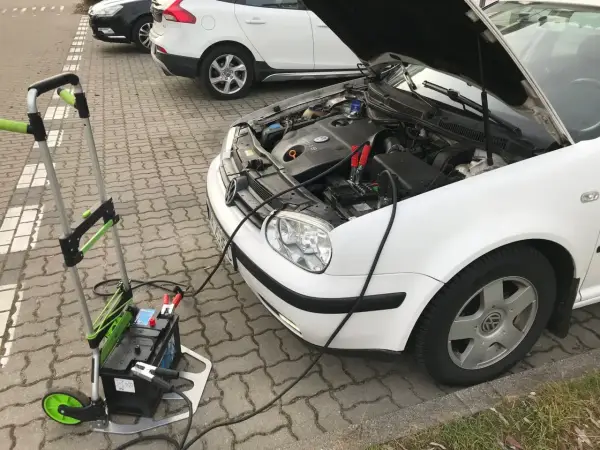 Awaryjny rozruch samochodu: podłączony wózek z akumulatorem do białego VW.