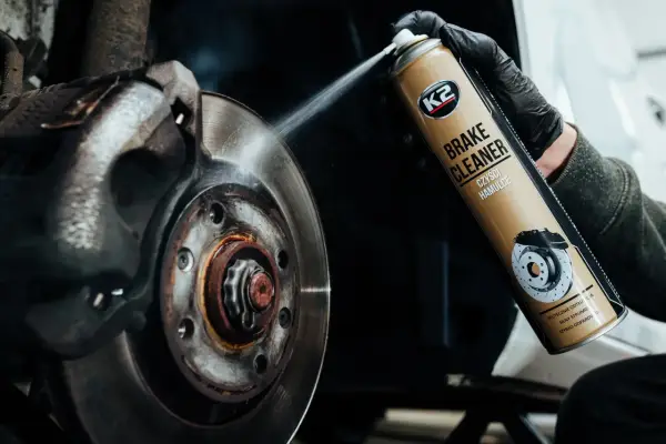 Czyszczenie hamulców: ręka w czarnej rękawiczce rozpyla preparat K2 Brake Cleaner na tarczę hamulcową.